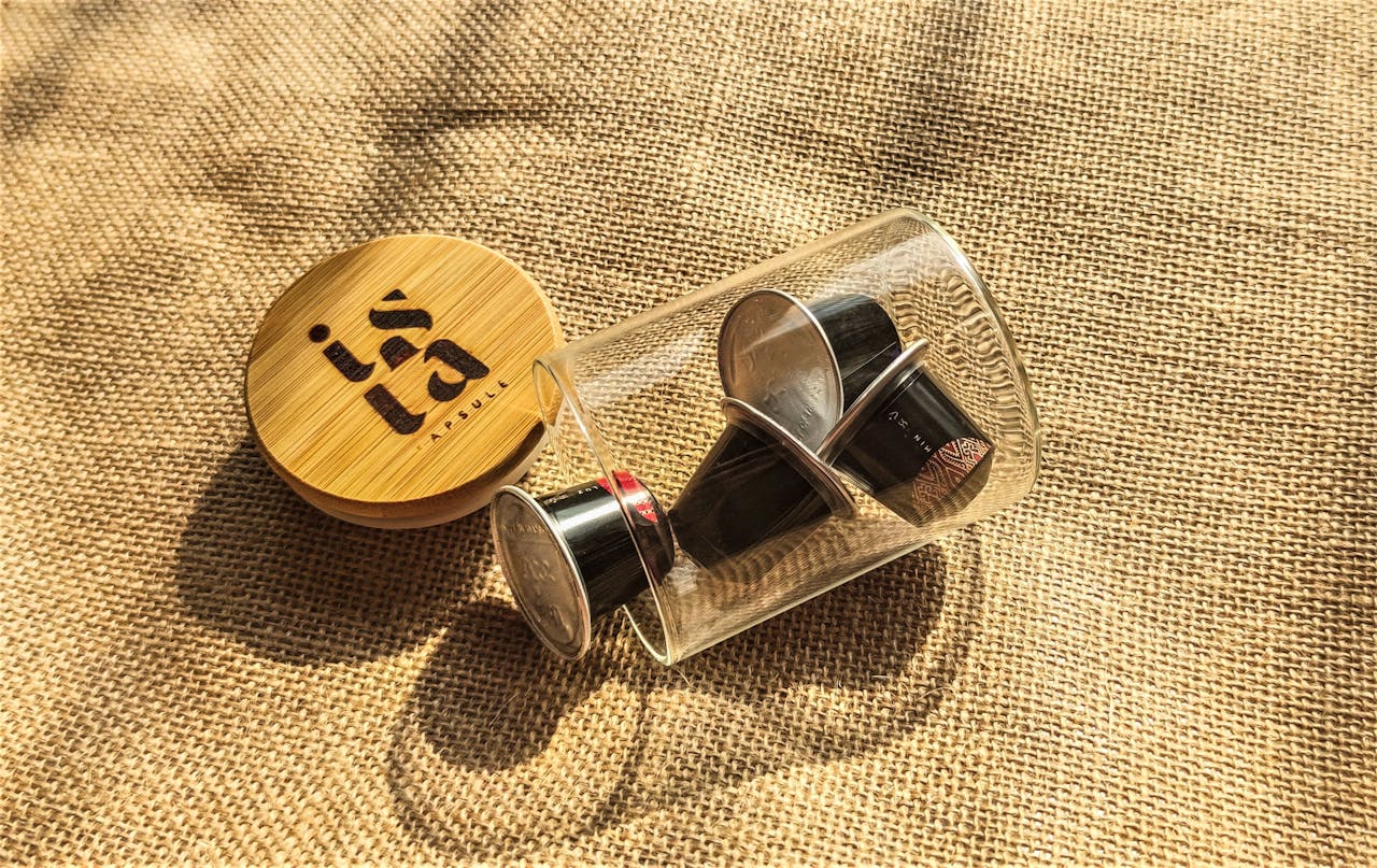 Reusable coffee capsule set inside a glass jar with bamboo lid on burlap. Eco-friendly concept.